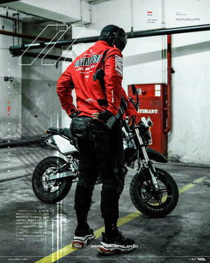 Person in red jacket and black pants standing next to a motorcycle in an industrial setting