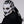 Person wearing a white and black mask with gold accents on a gray background