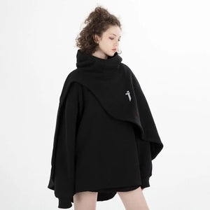 Person wearing a black poncho with a small white logo on a white background