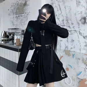 Person wearing a black outfit with unique designs, taking a mirror selfie in a room.