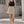 Kvinde i den lyse kaffefarvede A-formede tennisskort med en sort cropped top, set forfra udendørs