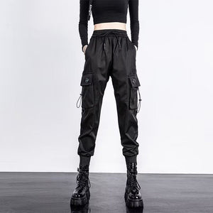 Black toggle Ankle Cuff Techwear Joggers, front view on a woman with a crop top, cargo pockets and platform boots