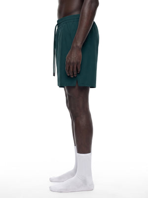 Sidevisning af de dybturkise forede gymshorts på en model, med langt snøre og splittet sidekant