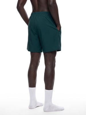 Dybturkise forede gymshorts set bagfra i tre kvarts vinkel på en model, med hånden i sidelommen
