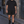 Man walking down a stone street in the Black Baggy Lined Gym Shorts and black tee, front view with logo