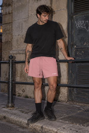 Pink baggy lined gym shorts worn with a black tee by an iron railing, front view of the drawstring waist