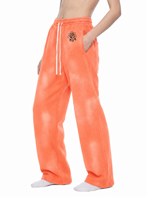 Orange wide leg sweatpants in three-quarter front view, one hand in the side pocket, drawstring hanging loose