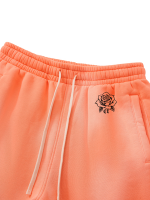 Close-up of the Orange sweatpants waistband: elastic waist, white drawstring and small black rose print