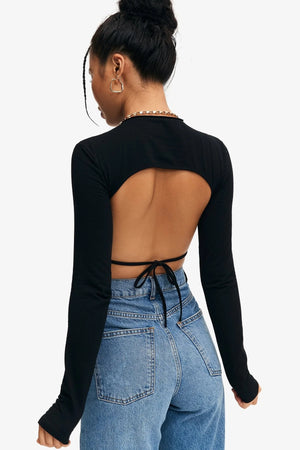 Back view of the black long sleeve crop top, bare upper back and a thin black tie over high-waisted jeans