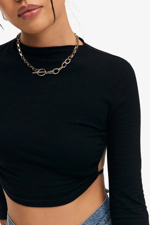 Close-up of the black long sleeve crop top neck and shoulder with a chain necklace, the curved hem at the waist