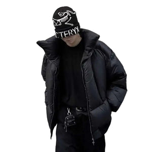 Person wearing a black puffer jacket and beanie with a logo on a gray background