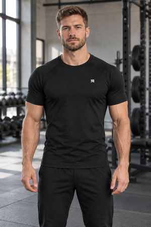 Mand i den sorte kortærmede kompressionstrøje i et fitnesscenter, set forfra med et lille hvidt emblem på brystet