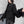 Γυναίκα με το oversized μαύρο δαντελωτό top να σηκώνει μία φραμπαλά μανσέτα, με φούστα από PU δέρμα και πέτρινο τοίχο πίσω της