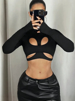 Czarny crop top z półgolfem noszony z czarnymi spodniami, widok z przodu z rękami skrzyżowanymi na wyciętym panelu na piersi