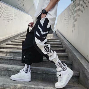 Chevron Panel Techwear Pants worn on concrete steps, black and white arrow panels down the leg and a cuffed hem