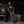 A model leans against a parked vehicle in a workshop wearing the black tank with wide printed trousers