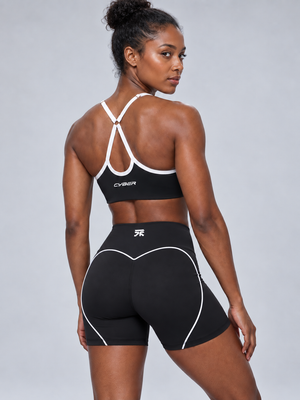 A model wears the black booty shorts from behind, the white heart trim curving over the seat