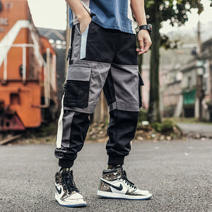 Black colorblock pants with grey panels worn by a train, front view, cargo pocket patches and cuffs