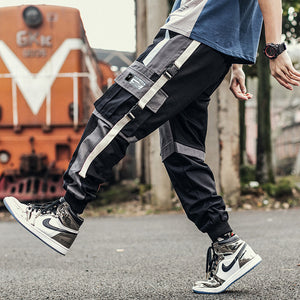 Black and grey colorblock cargo pants in side view while walking, hanging beige strap and jogger cuffs