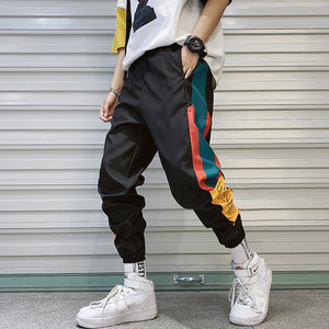 Black Colorblock Techwear Joggers worn in three-quarter view, hand in pocket, teal and red stripes and yellow panel