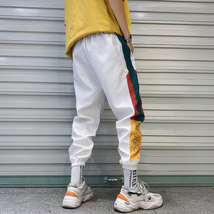 Hvide baggy colorblock-joggers set bagfra på skrå, med sidestriber og gult panel over manchetterne