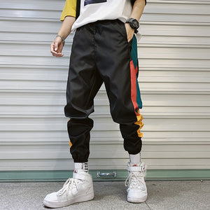 Black Colorblock Techwear Joggers in front view, baggy legs, teal and red stripes and white high-top sneakers