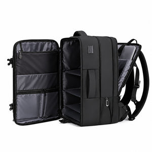 Commuter Techwear Backpack in black opened like a suitcase beside a laptop, tablet, cap and clothes