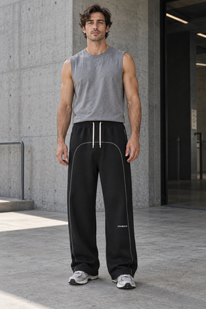 Man in a grey tank top and the Contrast Stitch Black Baggy Sweatpants, front view against a concrete wall