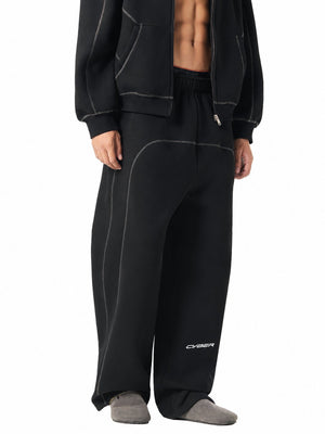 Three-quarter front view of the black oversized sweatpants, curved contrast seam and CYBER logo near the hem