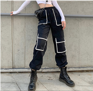Woman in the black Contrast Trim Y2K Cargo Pants by a concrete wall, front view with white-trimmed pockets