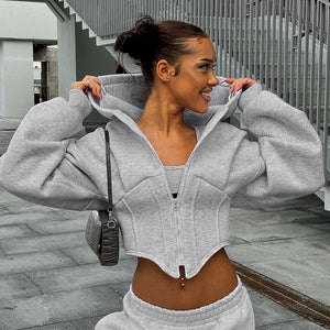 Smiling woman in the grey corset hoodie with a handbag, front view, cropped hem over grey joggers