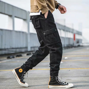 Black cropped cargo joggers in side view while walking, button flap thigh pocket and banded ankle