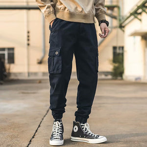 Man wearing the Cropped Cargo Cyberpunk Pants with a sweatshirt, front view, flap pocket and ankle cuffs
