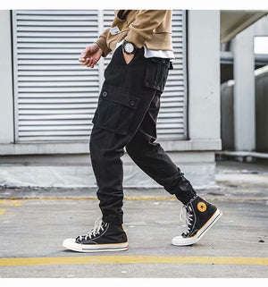 Black baggy cargo pants in side view while walking, oversized thigh pocket and elastic ankle cuff