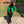 Green cropped denim jacket over a black top and black jeans, front view on a sunny campus walkway