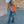 Orange cropped denim jacket over a white tee with ripped flared jeans, side view on a gravel terrace