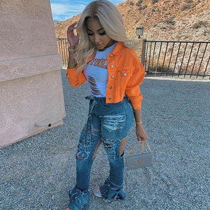Orange cropped denim jacket over a white tee with ripped flared jeans, side view on a gravel terrace