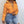 Cropped Puffer Y2K-jakke i orange båret halvt lynet op, nærbillede forfra med højtaljede jeans med flænger