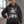 Model with a hand on the hip in the faded black hoodie by a window, front view of the stacked eyes print