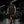 A model wears the black colourway in a gym, carrying a weight plate, chest print clearly visible