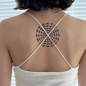 Woman's upper back in a white tank top with a black spider web temporary tattoo between the shoulder blades