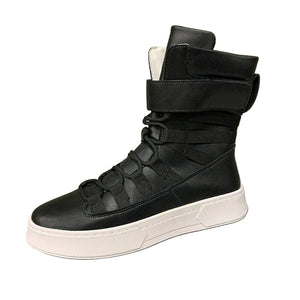 Black high-top sneaker with white sole on a gray surface and green background