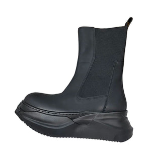 Black boot on a white surface with a beige box in the background