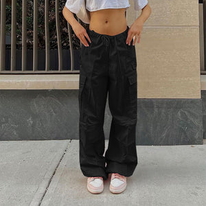 Black parachute y2k pants on a woman in front of a stone wall, front view of the baggy cargo legs and sneakers