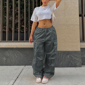 Grey parachute cargo pants worn low on the hips, front view with one arm raised and pink and white sneakers