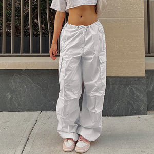 White drawstring parachute pants on a city sidewalk, front view of the baggy legs and large flap cargo pockets