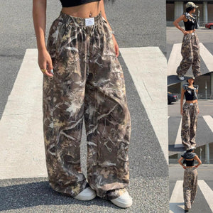 Spodnie bojówki Forest Camo na modelce w krótkim topie, widok z przodu, szerokie nogawki w kamuflażu z gałęziami z miniaturami z boku