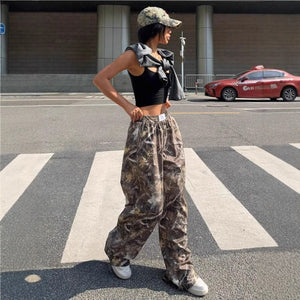 Widok z boku spodni bojówek Forest Camo, dłonie na biodrach, luźne szerokie nogawki opadające na sneakersy