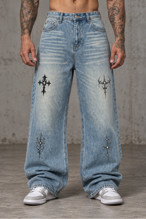 A tattooed model wears the light wash baggy jeans with grey trainers, gothic motifs on thighs and shins