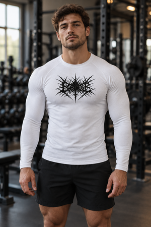 A man stands in a gym in the white long sleeve compression shirt, the knit tight over the arms